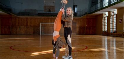 Two girls having fun practicing gymnastics in a sunny indoor sports hall.