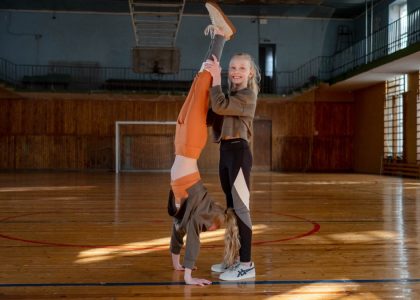 Two girls having fun practicing gymnastics in a sunny indoor sports hall.