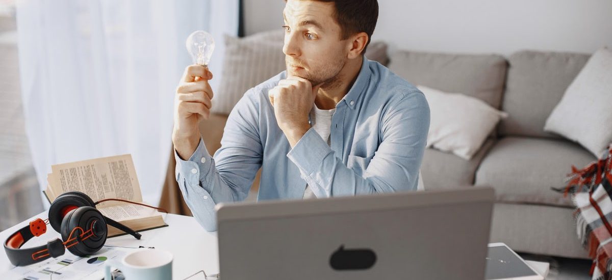 Young man at home desk holding a lightbulb, symbolizing a moment of inspiration during remote work.