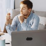 Young man at home desk holding a lightbulb, symbolizing a moment of inspiration during remote work.