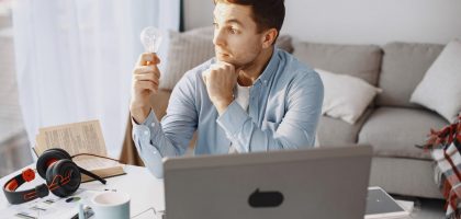 Young man at home desk holding a lightbulb, symbolizing a moment of inspiration during remote work.