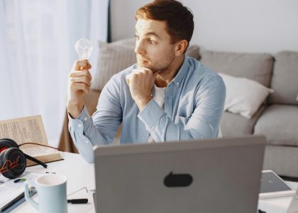 Young man at home desk holding a lightbulb, symbolizing a moment of inspiration during remote work.